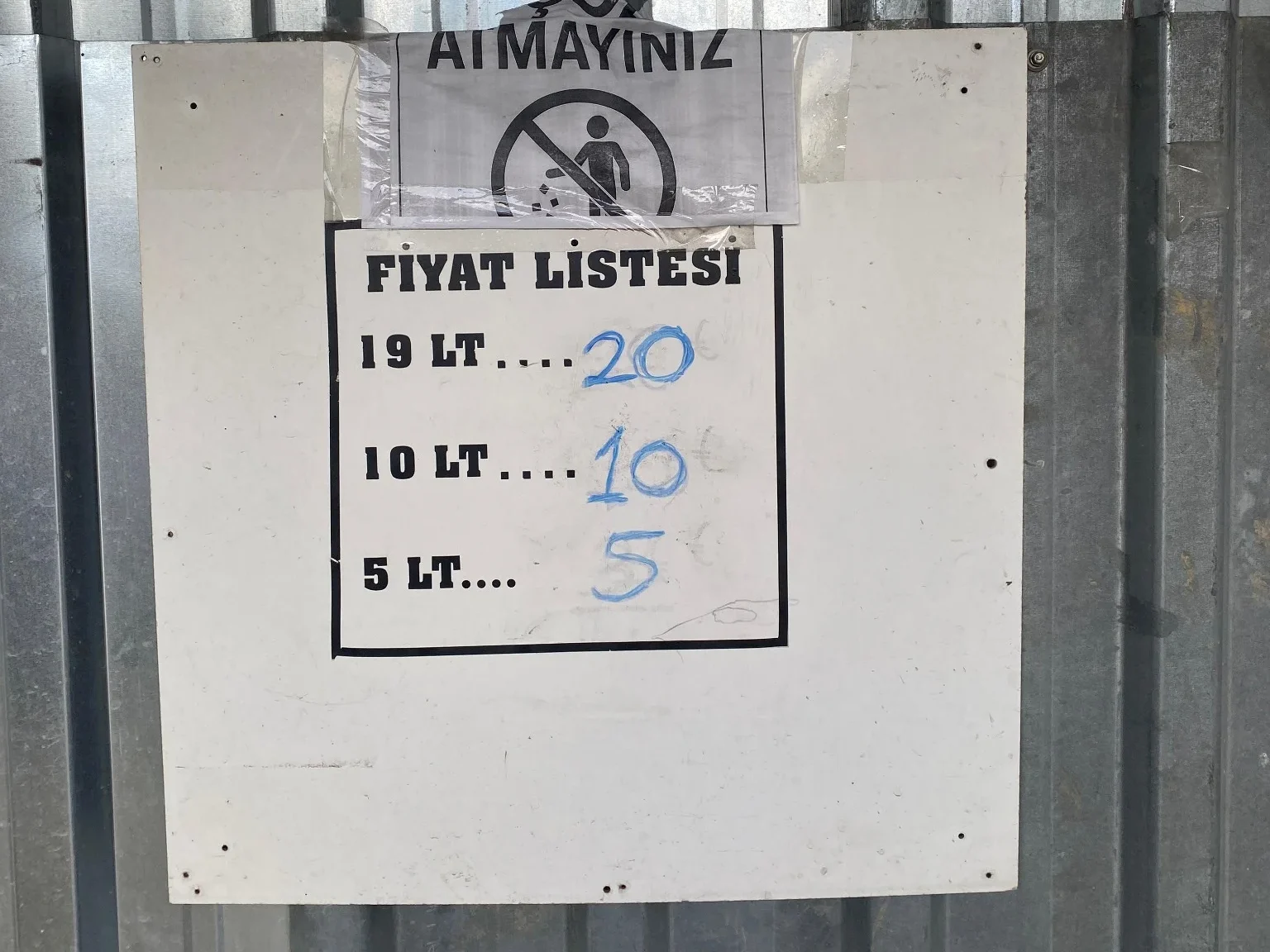 Çatalca Kalfaköy Su Kaynağı: Damacana Doldurma Noktaları ve Fiyatlar 7 Metal sac duvara asılmış bir tabela görünüyor. Üzerinde “Fiyat Listesi” başlığı altında 19 LT = 20 TL, 10 LT = 10 TL, 5 LT = 5 TL yazıyor. Üst kısımda ayrıca “Çöp atmayınız” ve “Ödemeyi karşı tarafa yapınız” uyarı yazıları var.
