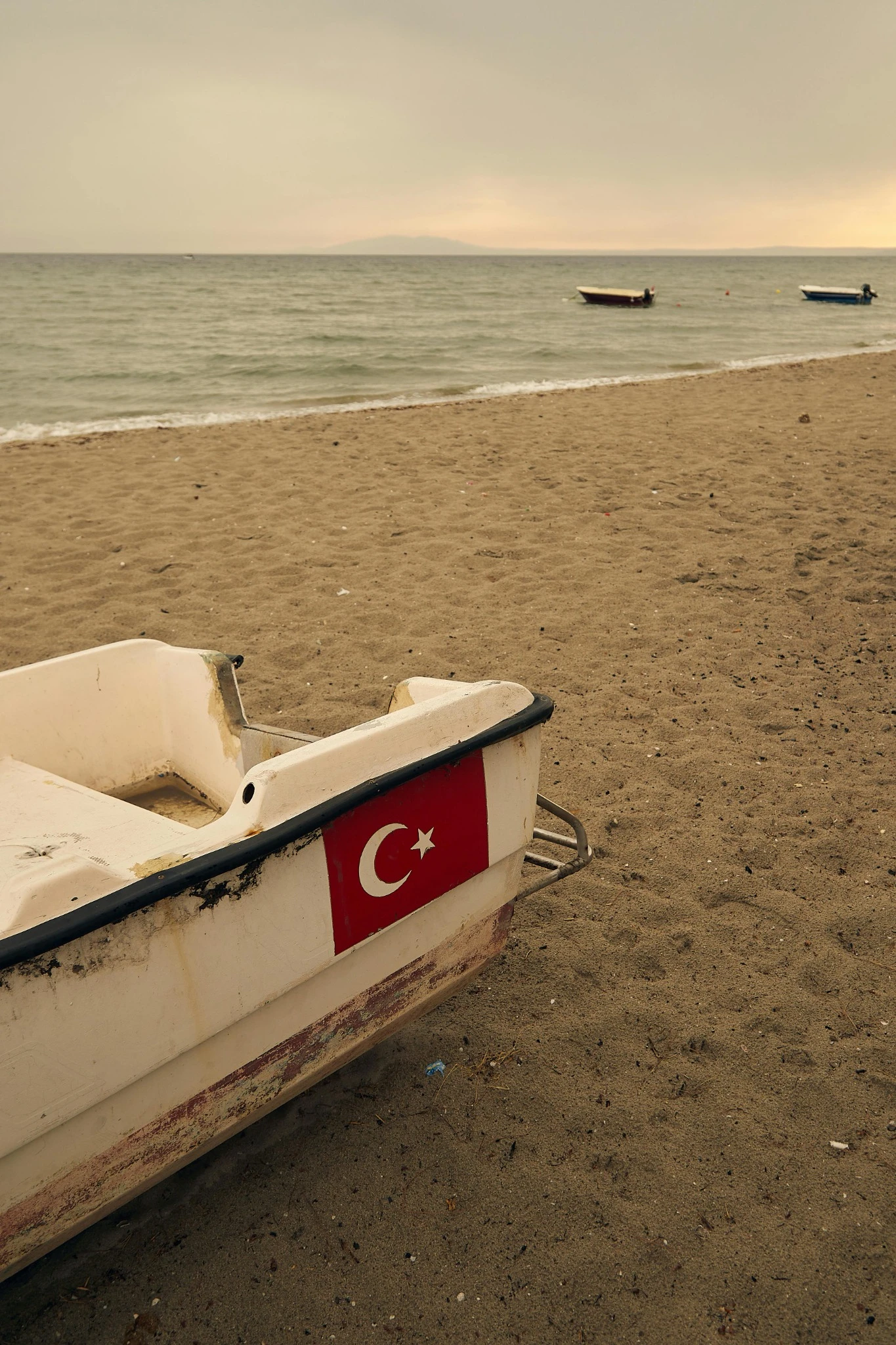 Çatalca’da Yazın Gidilecek Plajlar 5 Çatalca sahilinde kıyıya çekilmiş Türk bayraklı küçük bir tekne, kum plaj ve denizde duran iki balıkçı teknesi.