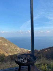 Tekirdağ Gezilecek Yerler Rehberi: Tarih, Doğa ve Manzara 15 Yanan odunlarla dolu bir mangal, arka planda Karadeniz manzarası ve kıvrımlı bir sahil yolu eşliğinde doğa ile iç içe huzurlu bir atmosfer sunuyor.