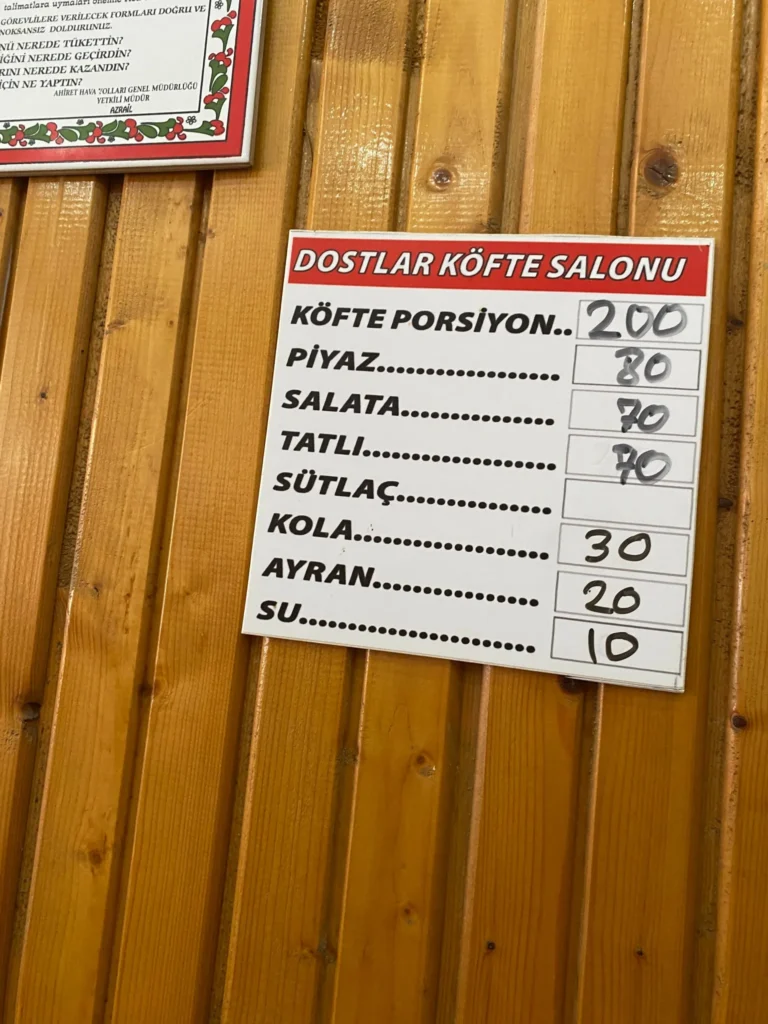 Çatalca'da En İyi Köfte Nerede Yenir? (2025 Güncel Rehber) 7 Dostlar Köfte Salonu'nun ahşap duvardaki menü panosu, köfte porsiyonu, piyaz, salata, tatlı ve içecek fiyatlarını gösteriyor